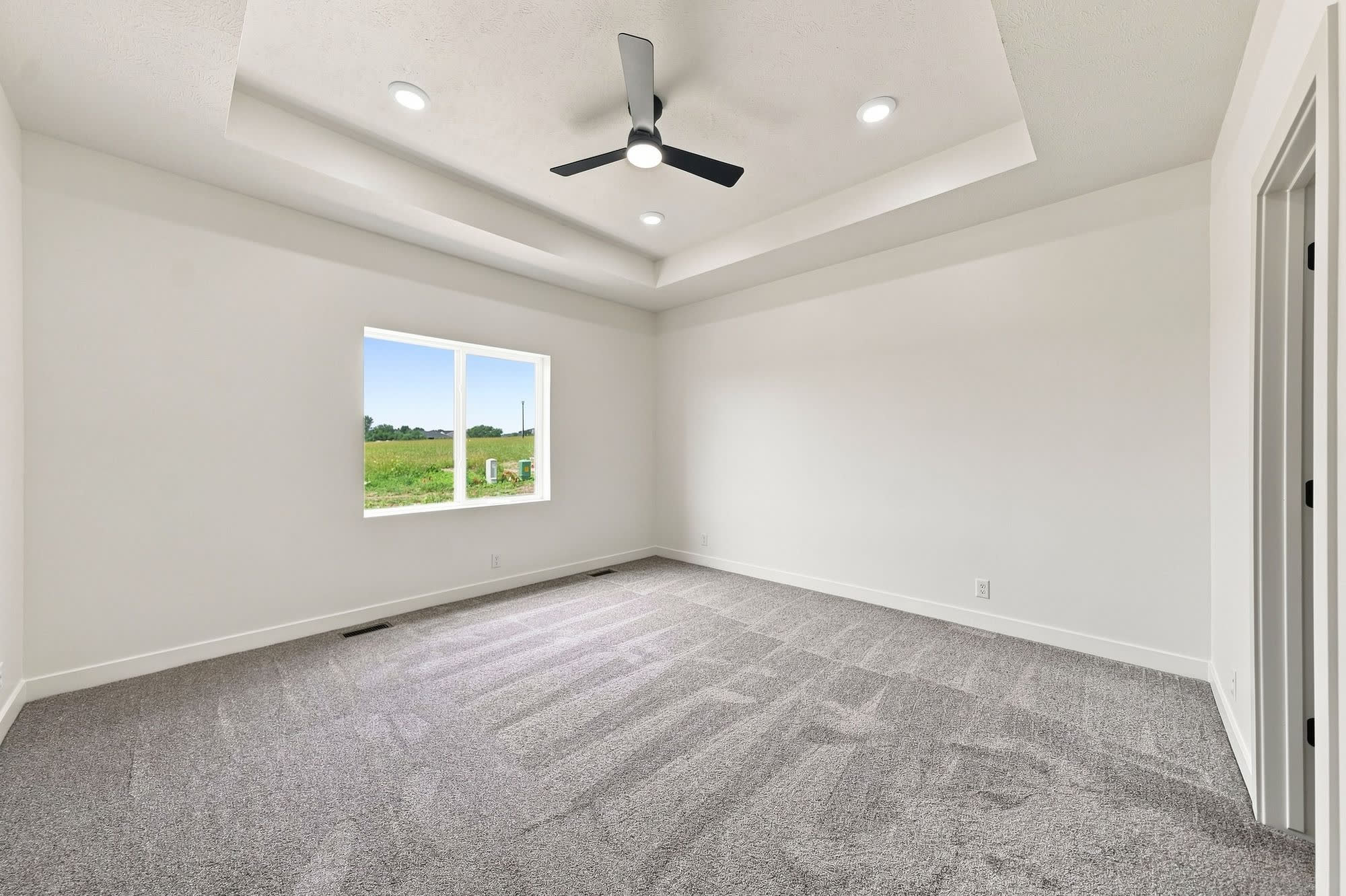 Empty primary bedroom with a tray ceiling and carpet.